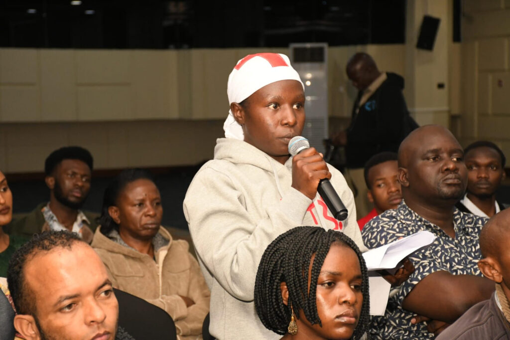 Harriet Afandi wearing a grey hoodie, and a white scarf as she speaks in a gathering at Nairobi