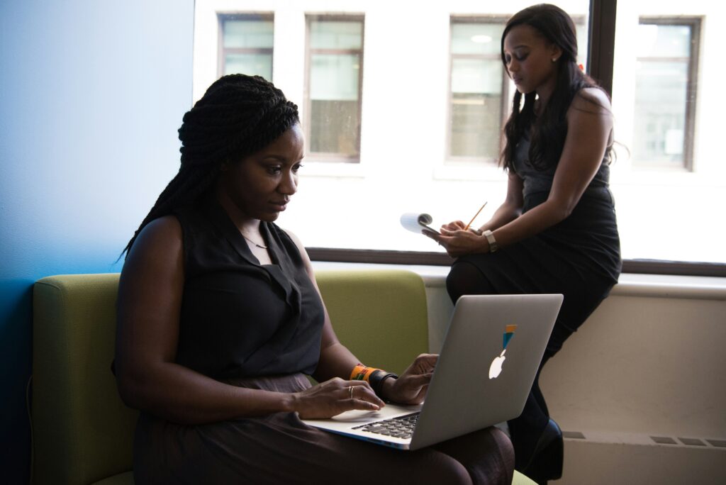 Two women in black outfits with one working on her system and the other taking a note.