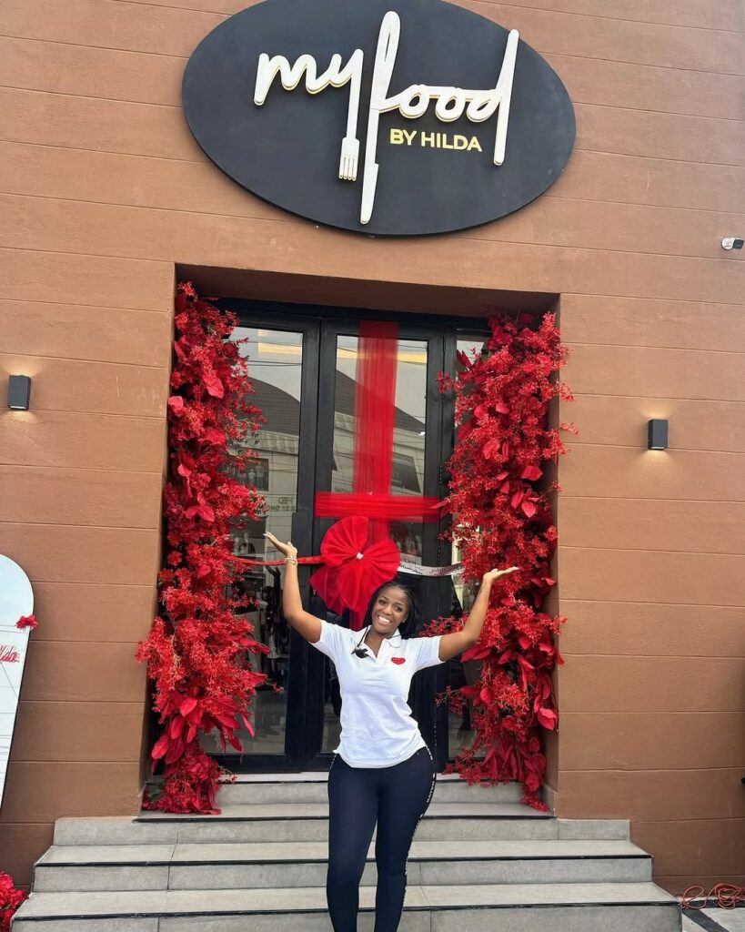 Hild Baci in a white top and black trouser standing in front of her newly opened resturant