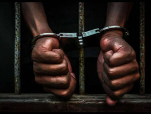 A man hands cuffed behind bars.