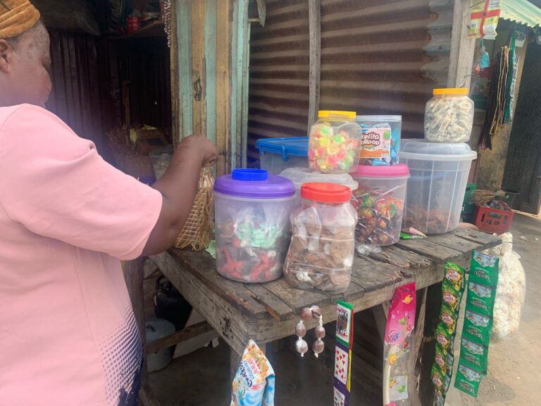 A woman in a plain pink cloth arranges snacks on a table in a stall.